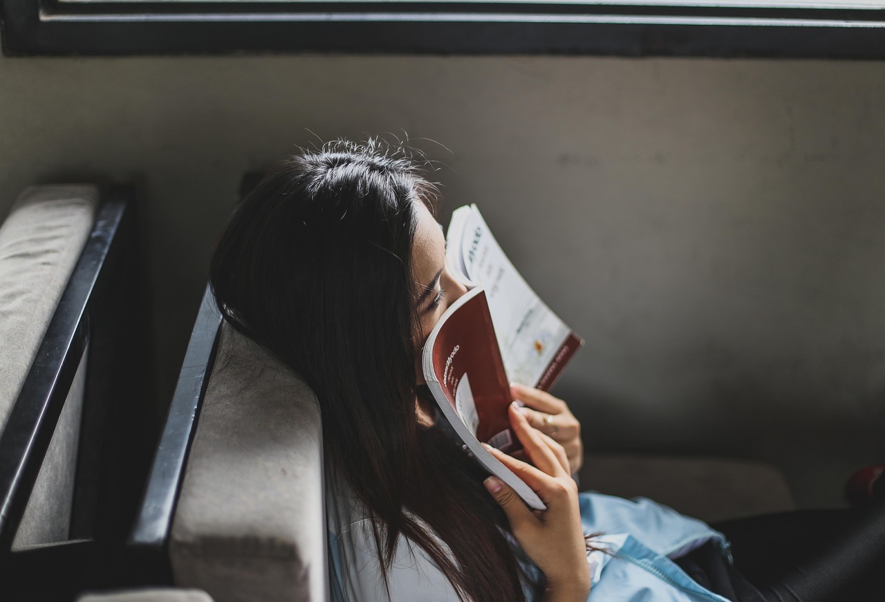 Nicht abschalten können: Erschöpfte Frau lehnt auf einem Sofa und versucht, mit einem Buch abzuschalten.