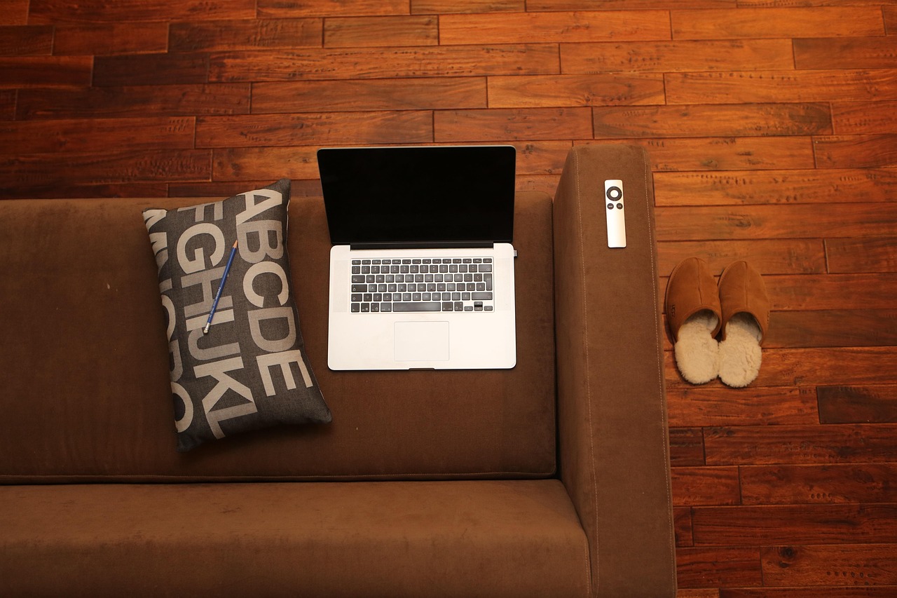 Laptop auf einem Sofa neben Hausschuhen – Übergang von der Arbeit in den Feierabend.
